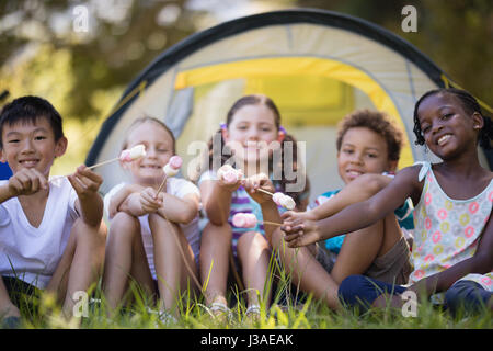 Portrait of happy friends montrant des bonbons tout en restant assis devant tente de camping Banque D'Images