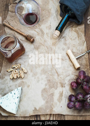 Vin et apéritif set avec copie espace dans le centre. Verre de vin rouge, bouteille, corkscrewer, fromage bleu, les raisins, le miel, les noix sur du papier craft huileux sur table en bois rustique, vue du dessus. Banque D'Images