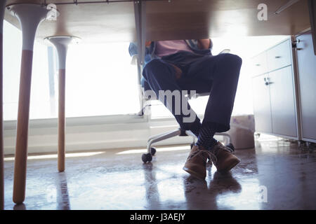 La section basse de businessman sitting on chair at desk in office Banque D'Images