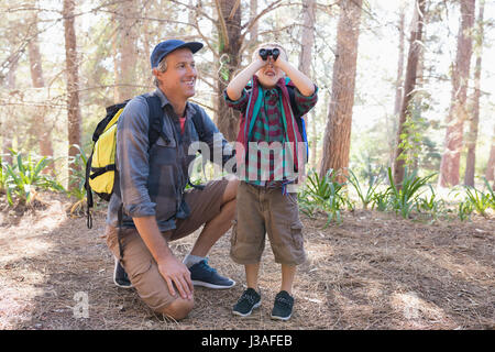 Mature man watching boy looking through binoculars in forest Banque D'Images