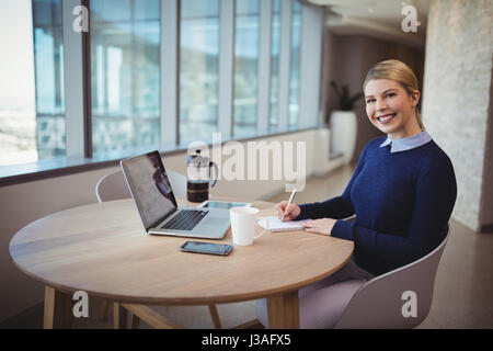 Portrait of smiling female executive écrit sur le bloc-notes in office Banque D'Images