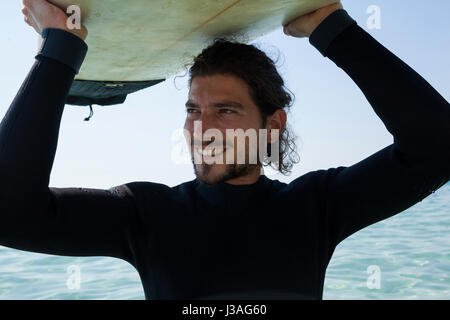 Smiling internautes en transportant plus de surf wetsuit tête à plage côte Banque D'Images