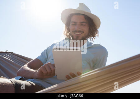 Smiling man relaxing on hammock et using digital tablet sur la plage Banque D'Images