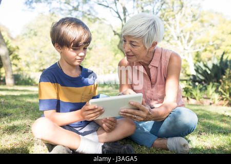 Grand-mère et petit-fils using digital tablet dans le parc aux beaux jours Banque D'Images