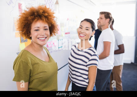 Portrait of smiling business people standing par tableau blanc avec des collègues en arrière-plan Banque D'Images