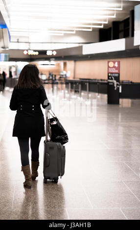 Curly moderne femme modèle en manteau noir et des bottes avec une valise et un sac à main modèle passe à l'aéroport de hall à bord de l'avion et l'enregistrement. Banque D'Images