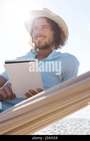 Smiling man relaxing on hammock et using digital tablet sur la plage Banque D'Images