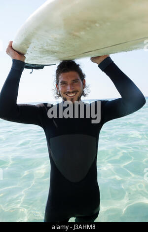 Portrait of smiling surfer dans l'exécution de combinaisons de surf la plus tête à plage côte Banque D'Images