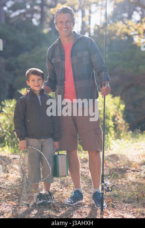 Portrait de l'heureux père et fils avec la canne à pêche standing in forest Banque D'Images
