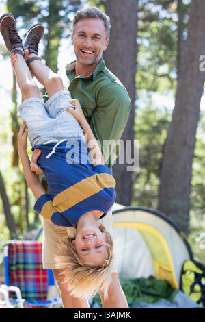 Portrait of cheerful father holding fils à l'envers au camping Banque D'Images