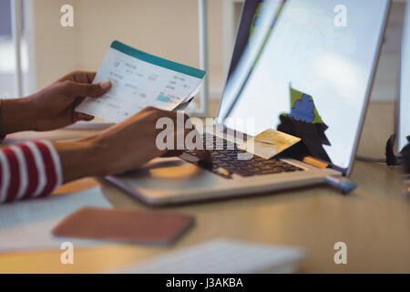 Les mains coupées de businesswoman holding documents while using laptop in office Banque D'Images