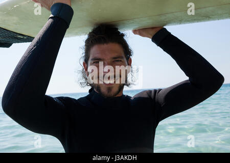 Portrait of smiling surfer dans l'exécution de combinaisons de surf la plus tête à plage côte Banque D'Images