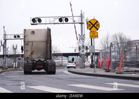 Un camion-tracteur semi sale sans remorque traverse un passage à niveau avec les panneaux d'avertissement et feux de circulation le long de la route avec la construction Banque D'Images