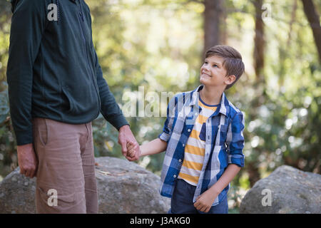 Section intermédiaire de père holding hand of smiling boy lors d'une randonnée en forêt Banque D'Images