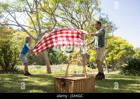 Père et fils se propager la couverture de pique-nique dans le parc Banque D'Images