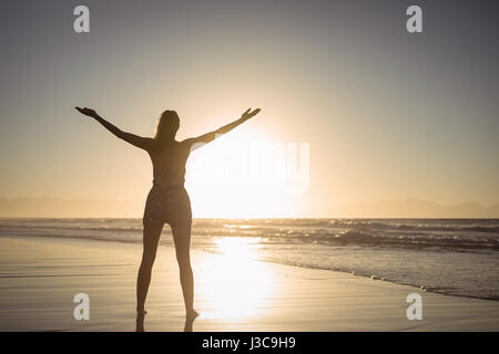 Vue arrière de l'ossature woman with arms outstretched standing at beach pendant le crépuscule Banque D'Images