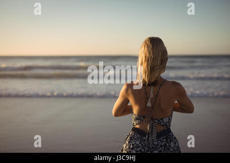 Rear view of woman doing yoga at beach pendant le crépuscule Banque D'Images