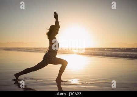 Vue latérale d'ossature woman doing yoga sur le rivage à plage pendant le crépuscule Banque D'Images