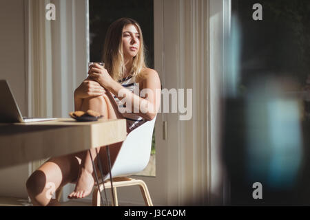 Thoughtful woman sitting on chair et holding Coffee cup à la maison Banque D'Images