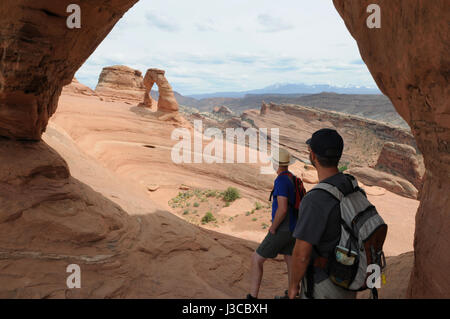 Deux randonneurs se tourner vers la délicate Arche dans un autre arch dans Arches National Park, Moab, Utah. Banque D'Images