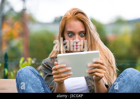 Choqué young woman making funny faces à une tablette numérique, voyant quelque chose de surprenant sur l'internet Banque D'Images