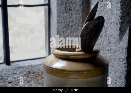 Cuillères de cuisine en bois dans un grand pot en céramique ou en pot, avec des murs en pierre et fenêtre en arrière-plan Banque D'Images