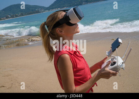 Jolie femme portant des lunettes de réalité virtuelle debout sur la plage avec télécommande de drone sur fond de mer Banque D'Images