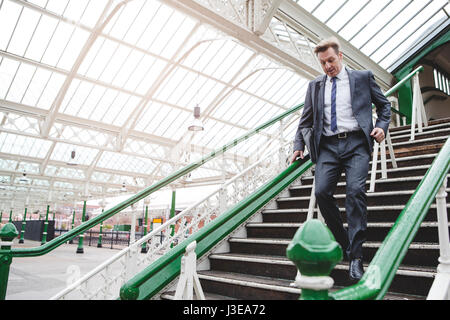 Homme d'affaires formel fonctionnant en bas de l'escalier pour attraper son train à la gare. Il a un sac sur son épaule. Banque D'Images