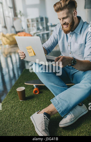 Homme barbu souriant assis sur planche et using laptop Banque D'Images