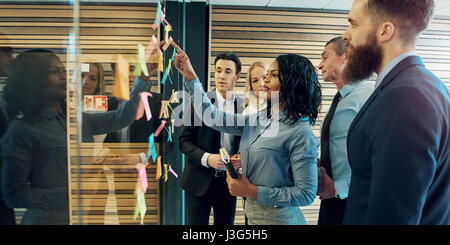 Groupe de gens d'affaires créatifs mettant brainstorming notes adhésives sur verre wall in office Banque D'Images