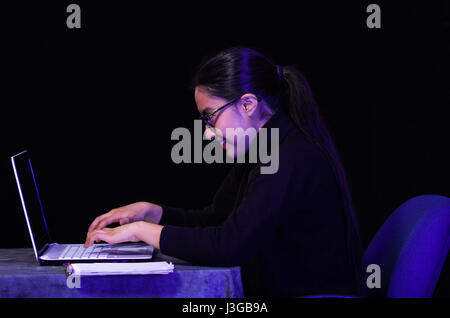 Portrait d'une belle, heureuse et smart girl travailler avec son ordinateur portable sur fond sombre à l'aide de verres Banque D'Images