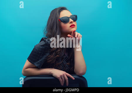 Portrait de la belle jeune femme, dans les verres sur le vintage noir robe à pois sur fond bleu. Jeune modèle féminin. Banque D'Images