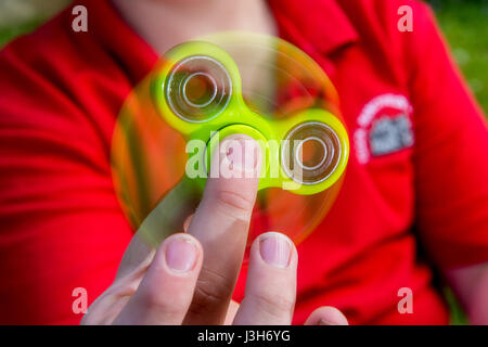 Un jeune garçon dans un uniforme de l'école rouge joue avec un jouet vert fidget spinner Banque D'Images