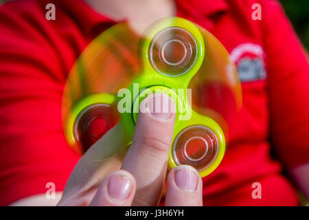 Un jeune garçon dans un uniforme de l'école rouge joue avec un jouet vert fidget spinner Banque D'Images