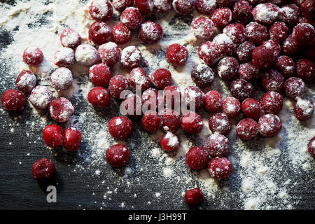 Beaucoup de cerises congelées sans bâtons sur un fond noir en bois.Des vitamines et une alimentation saine.saupoudrée de farine ou de sucre en poudre Banque D'Images