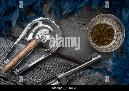 Thompson Fusil, revolver, cigare sur le cendrier en verre de whisky, et Blue Feather boa Banque D'Images