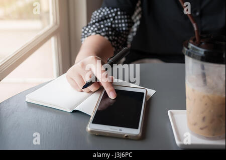 La femme de toucher sur l'écran du smartphone tout en écrivant quelque chose dans un café. Concept de travail de n'importe où Banque D'Images