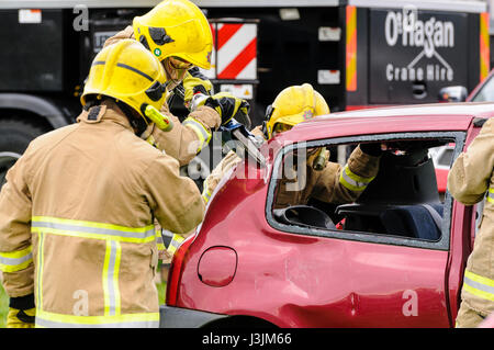 Firecrew de l'Irlande du Nord Service d'incendie et de sauvetage de démontrer comment utiliser l'équipement de coupe hydraulique pour libérer un conducteur qui était coincé dans une voiture après un Banque D'Images