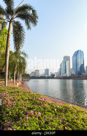 Parterre de fleurs, palmiers et promenade en bois au parc Benjakiti (Benjakitti) et les gratte-ciel modernes à Bangkok, Thaïlande. Banque D'Images