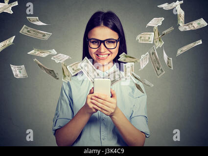 Transfert d'argent, la banque en ligne e-commerce concept. Happy young woman in glasses using smartphone avec des dollars de vol isolé sur l'écran Banque D'Images