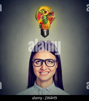 Manger sain des bouts de régime concept. Portrait d'une femme à la recherche jusqu'à l'ampoule électrique faites de fruits isolé sur fond de mur gris. Banque D'Images