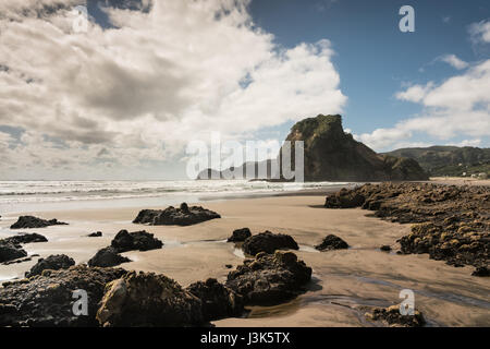 Auckland, Nouvelle-Zélande - mars 2, 2017 : le rocher du Lion sur Piha beach de mer de Tasman entouré de surf et sous le bleu ciel nuageux. Avant-garde est sable et dispe Banque D'Images