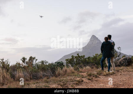 Jeune couple à l'extérieur regardant et suivi d'un drone volant dans le ciel au cours de la campagne. L'homme et la femme en utilisant la photographie pour drone dans la r Banque D'Images