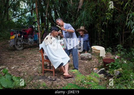 Yangshuo, Chine - le 2 août 2012 : Chinese man ayant une coupe de cheveux à l'extérieur dans une zone rurale à la périphérie de la ville de Yangshuo en Chine. Banque D'Images
