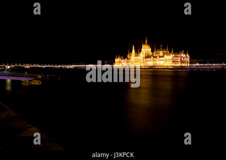 Le bâtiment du parlement hongrois éclairés la nuit, de l'autre côté de la rivière du Danube, avec les lumières se reflétant dans la rivière. Banque D'Images