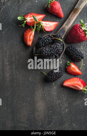 Fruits rouges sur fond de bois sombre. Fraises fraîches et mûres en cuillère de cuisine rustique