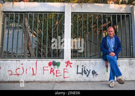 Photo d'un homme assis sur un mur sur lequel un graffitti peut être vu avec l'inscription 'gratuitement' la Libye, pris au centre-ville de Tripoli, Libye, 05 avril 2017. Le dictateur libyen Mouammar Kadhafi a été chassé hors de son palais il y a six ans, après quoi la ville s'est trouvée dans la carie. Photo : Simon Kremer/dpa Banque D'Images