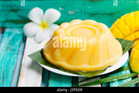 Pudding de mangue, gelée sur plaque blanche avec feuille de palmier. Fond en bois coloré. Banque D'Images