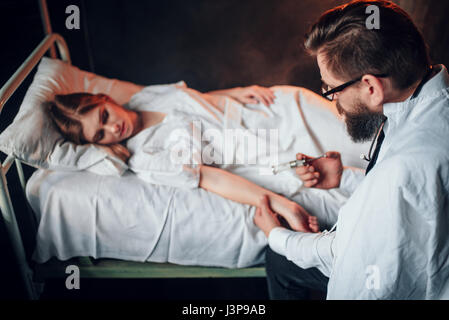 Médecin homme rend l'injection seringue de femme malade dans lit d'hôpital. La maladie du patient dans un centre de femmes, la récupération et le traitement de la santé Banque D'Images