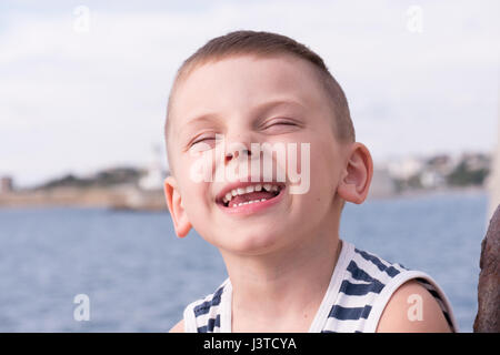 Rire cute little boy wearing striped shirt fermer les yeux avec plaisir Banque D'Images